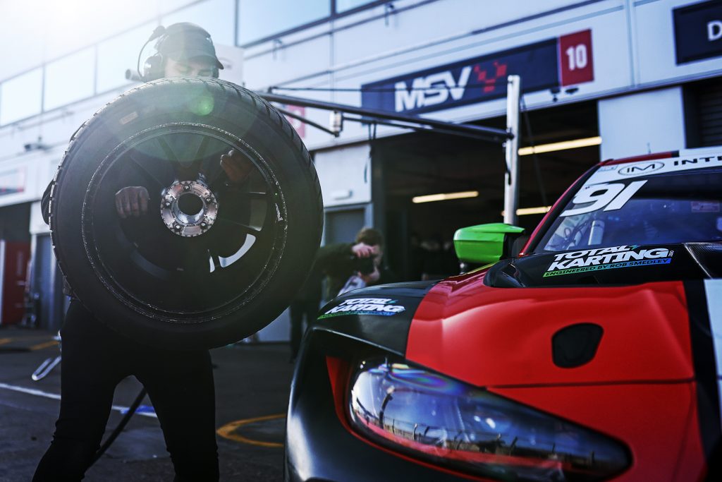 A mechanic carries a tyre to the #91 Century Motorsport BMW M4 GT3